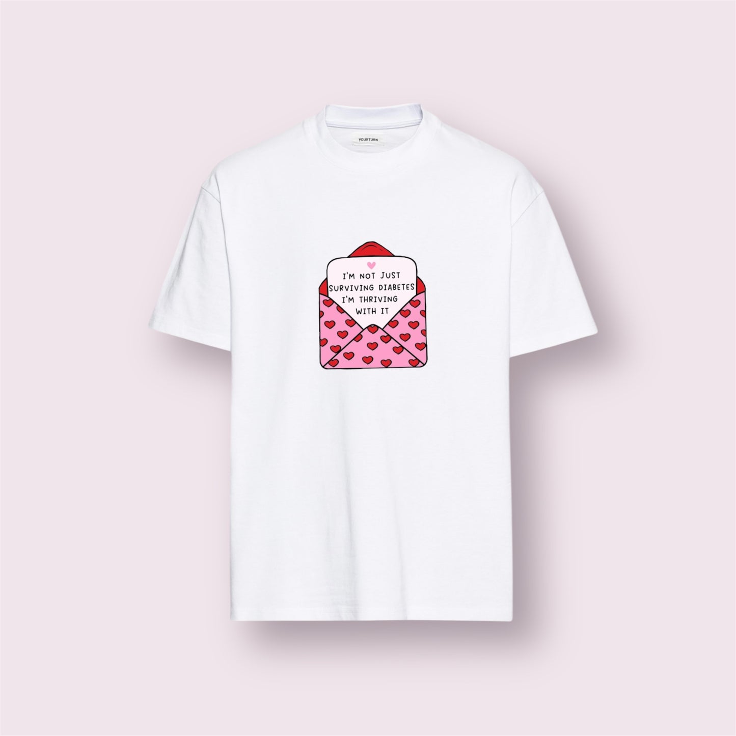 Camiseta blanca con ilustración de sobre rosa con corazones y mensaje "I'm not just surviving diabetes, I'm thriving with it", diseño positivo y original de Aroa Dedales