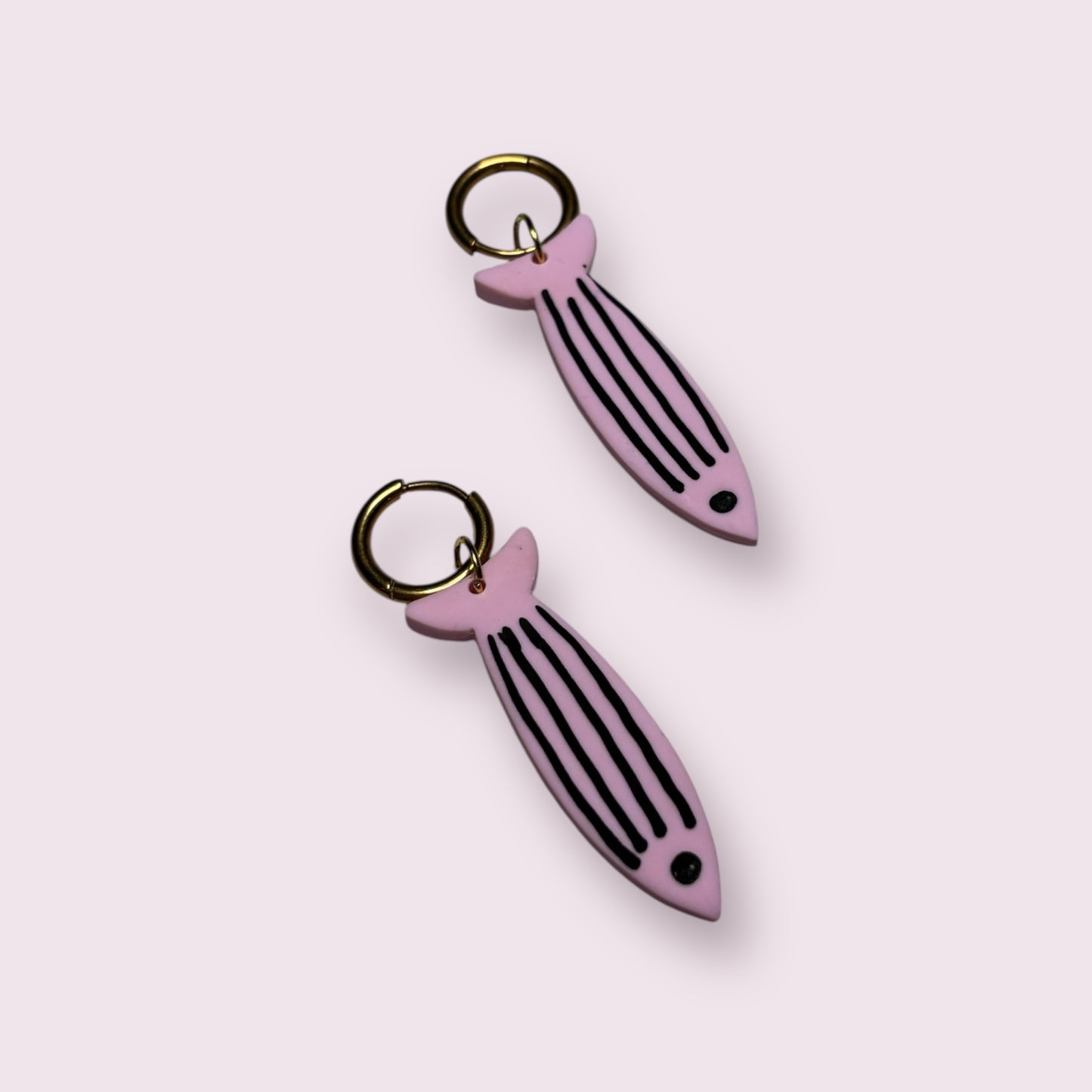 Pendientes con forma de sardina en color rosa pastel con rayas negras, hechos a mano en arcilla polimérica por Aroa Dedales. Diseñados con aro dorado, son el complemento perfecto para looks veraniegos con estilo marinero. Joyas artesanales originales, ligeras y divertidas, ideales para regalar o lucir en vacaciones. Hecho en España con acabado único y creativo para amantes del diseño costero.