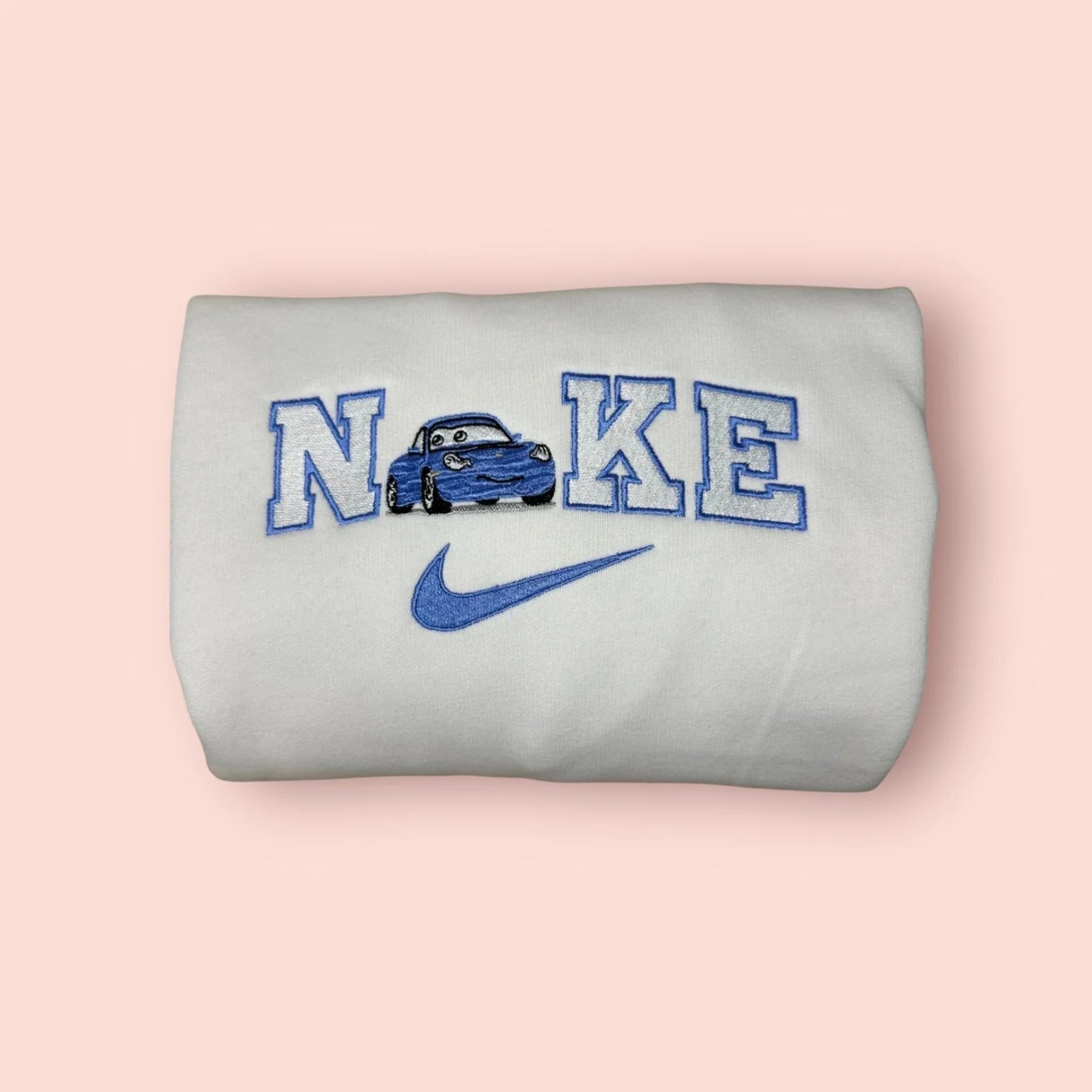 Sudadera blanca de alta calidad con un elegante bordado de Sally Carrera de la película Cars. El diseño presenta al Porsche azul integrado en letras estilo universitario con hilos a juego. Prenda de moda personalizada, perfecta para fans de Disney y Pixar. Ideal para regalar o para combinar con la sudadera de Rayo McQueen y crear el conjunto de pareja definitivo.