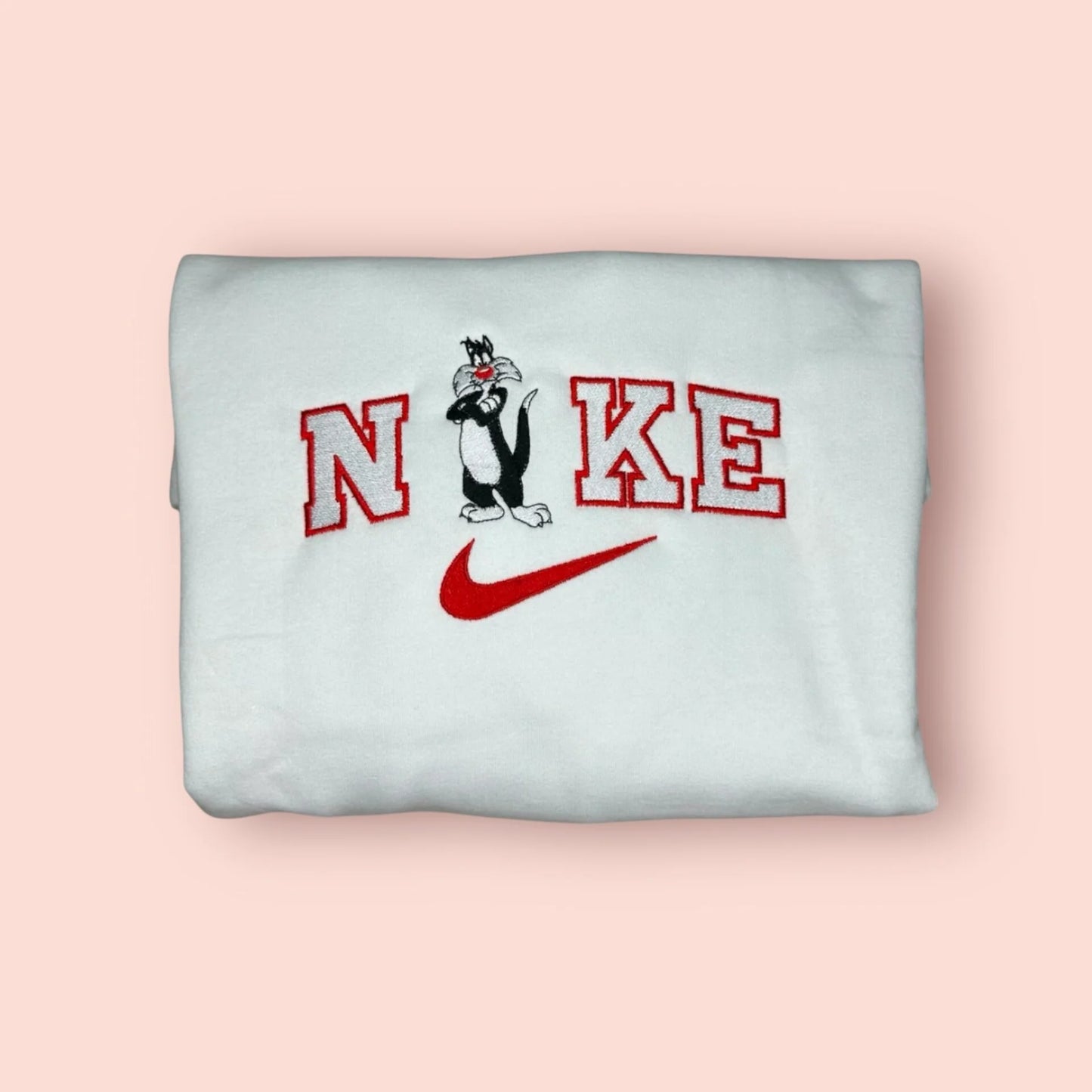 Sudadera blanca de estilo varsity con un bordado detallado del Gato Silvestre de los Looney Tunes. El diseño presenta al personaje con su clásica expresión de "haber visto un lindo gatito", integrado en letras rojas estilo universitario. Ropa personalizada de estética vintage y noventera (90s aesthetic). El regalo perfecto para nostálgicos de los dibujos animados clásicos o para combinar en pareja con la sudadera de Piolín. Tejido de algodón de alta calidad y bordado duradero.