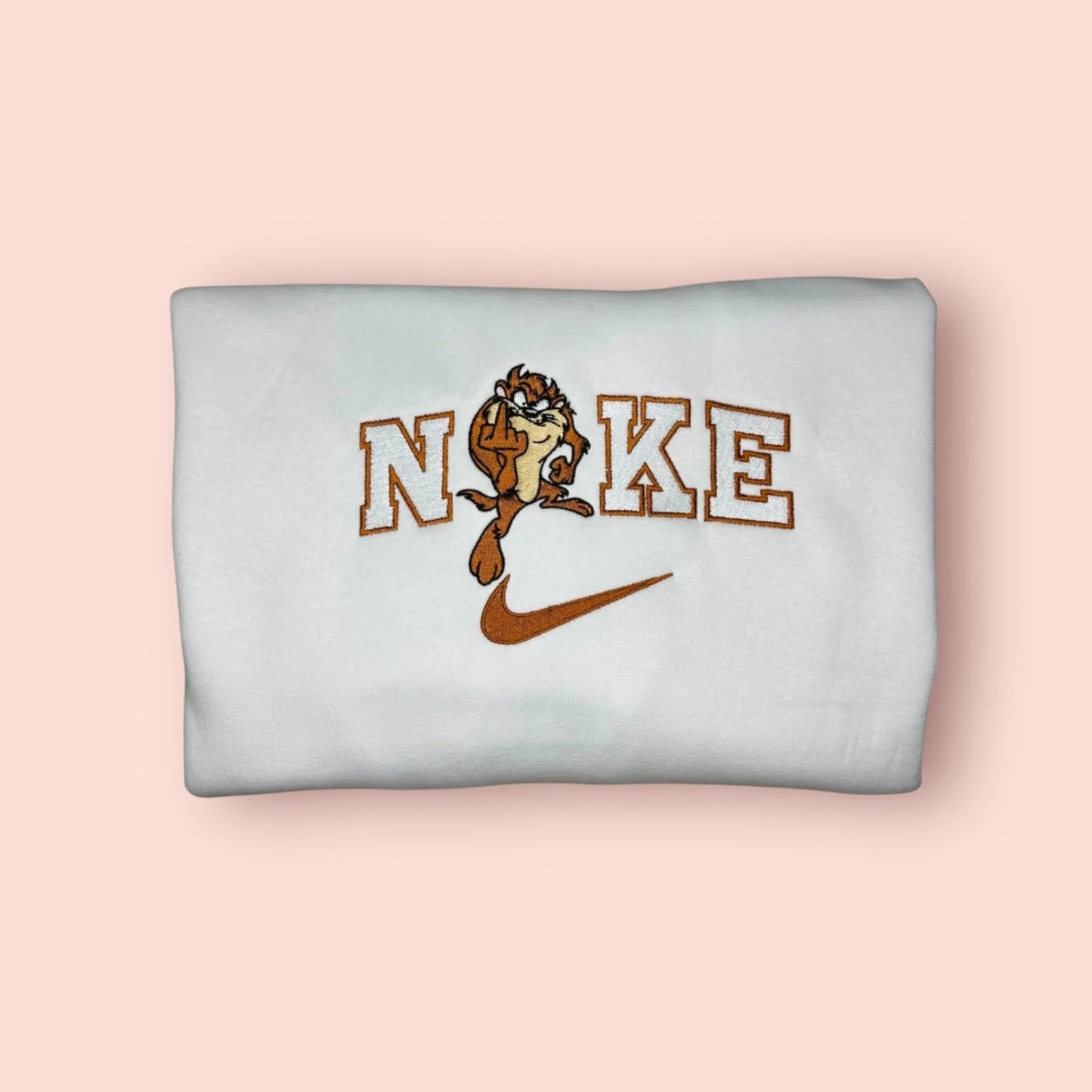 Sudadera blanca de estilo urbano con un bordado provocador de Taz, el Demonio de Tasmania. El diseño muestra al personaje de los Looney Tunes haciendo una peineta (dedo medio) con una expresión gamberra, integrado en letras estilo varsity. Ropa "streetwear" con actitud, inspirada en la moda rebelde de los 90 y los 2000. Ideal para regalar a amigos con un sentido del humor ácido o para llevar un outfit con mucha personalidad. Calidad premium y bordado resistente.