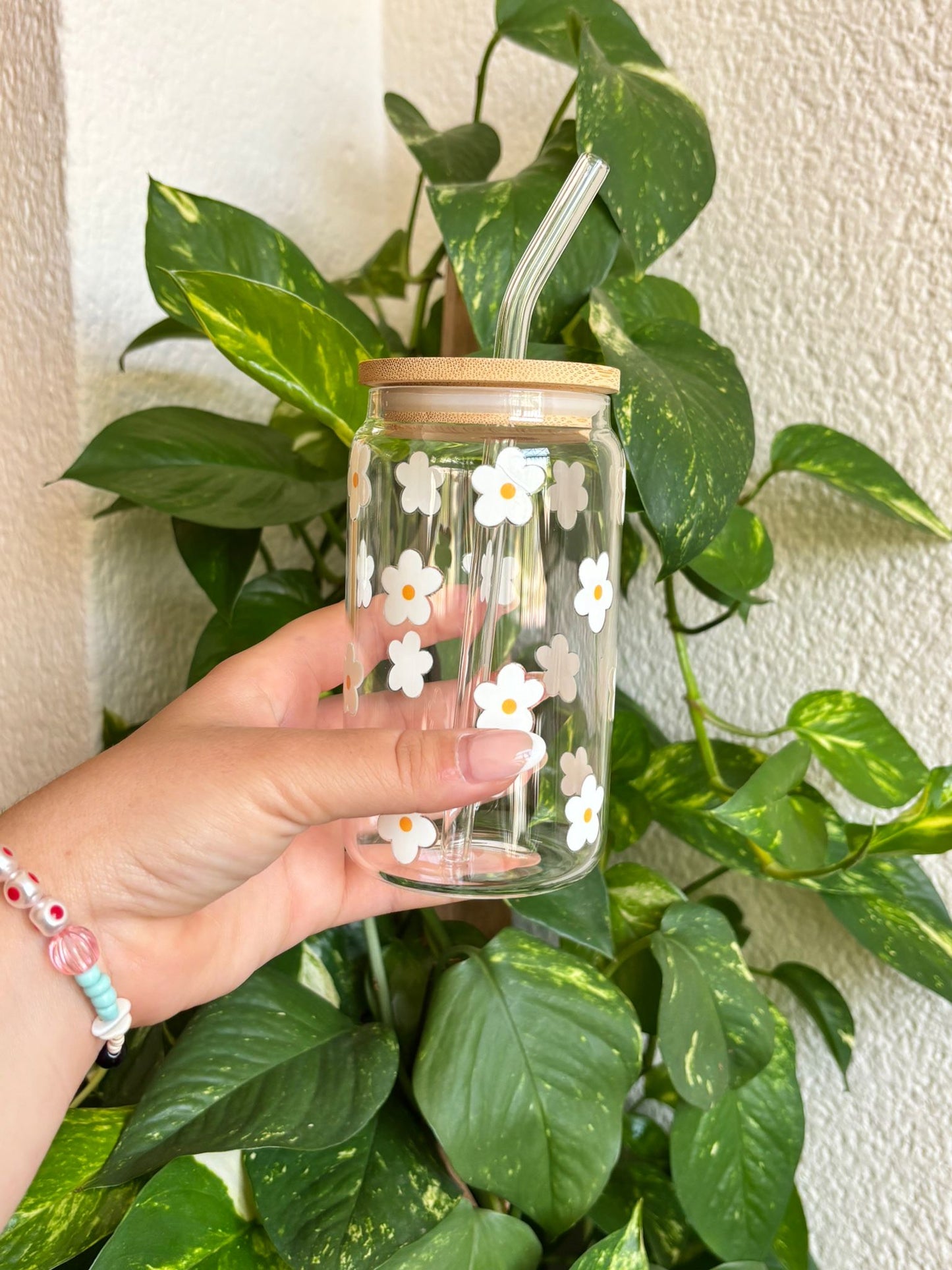 Vaso de cristal reutilizable decorado con margaritas blancas pintadas a mano, tapa de bambú natural y pajita de vidrio transparente. Diseño veraniego, ecológico y encantador para llevar tus bebidas favoritas como café con hielo, té frío, smoothies o agua con frutas. Ideal como regalo original y sostenible para amantes de las flores, la decoración bonita y el estilo natural. Perfecto para sorprender en cumpleaños, detalles de agradecimiento o para disfrutar de tus momentos de relax con estilo.