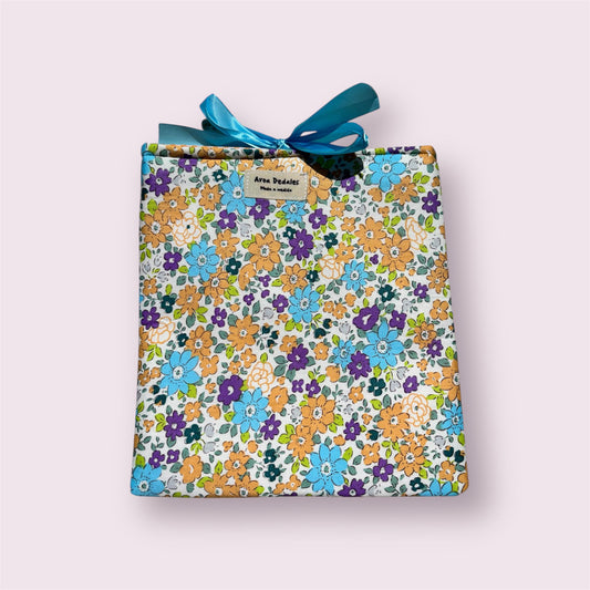 Funda de tela acolchada con estampado floral en tonos naranja, azul y violeta, decorada con lazo azul.