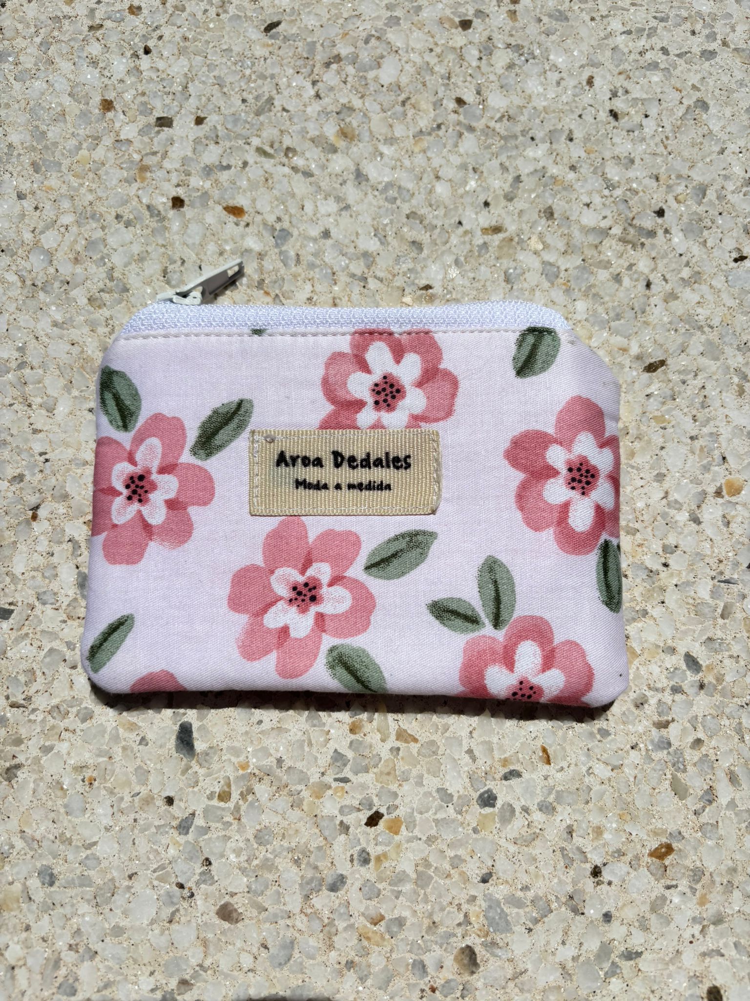 Monedero blanco con estampado de flores rosas y verdes, cierre de cremallera metálica, hecho a mano por Aroa Dedales. Ideal para uso diario o como regalo artesanal.
