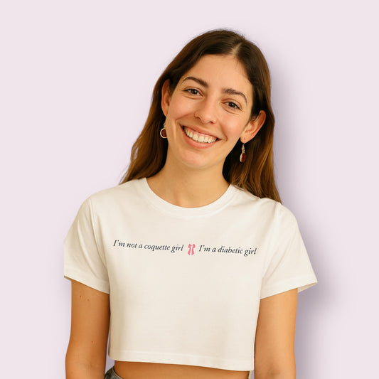 Mujer sonriente luciendo camiseta cropped blanca con el texto "I'm not a coquette girl, I'm a diabetic girl", ideal para jóvenes con diabetes que buscan ropa con mensaje, moda inclusiva y divertida para diabéticas tipo 1. Producto de Aroa Dedales