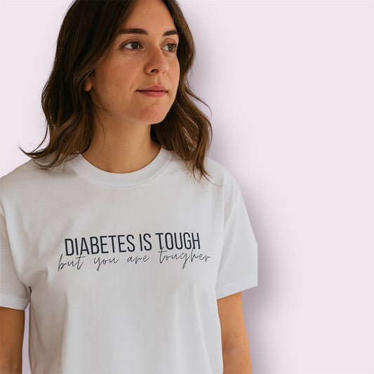 Camiseta blanca con la frase motivadora "Diabetes is tough but you are tougher", modelo mujer mirando de perfil, fondo rosa claro