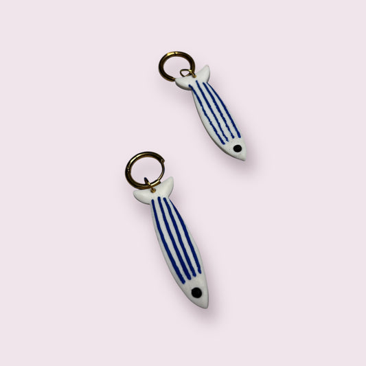 Pendientes artesanales Sardineta hechos a mano en cerámica blanca con rayas azules y forma de pez, con cierre de aro dorado. Diseñados por Aroa Dedales para amantes del mar, ideales como regalo original y complemento veraniego con estilo mediterráneo. Compra online piezas únicas de joyería artística.
