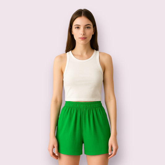 Mujer vistiendo pantalón deportivo tipo short verde brisa, con cinturilla elástica, ideal para look casual y cómodo en verano, moda femenina juvenil, fotografía para ecommerce de ropa, fondo rosa pastel que resalta el color del short.