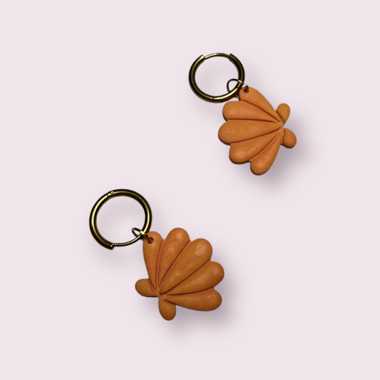 Pendientes artesanales con forma de concha en tono naranja terracota, hechos a mano en arcilla polimérica con cierre de aro dorado. Diseño exclusivo de Aroa Dedales, perfectos para looks veraniegos, escapadas a la playa o como regalo original y creativo. Joyería ligera, colorida y con estilo mediterráneo para lucir con personalidad.