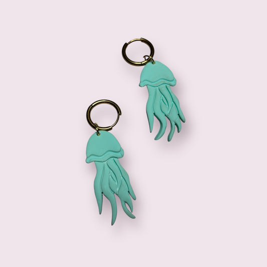 Pendientes artesanales con forma de medusa en color azul turquesa, elaborados a mano en arcilla polimérica y montados en aro dorado. Diseño original de Aroa Dedales ideal para looks frescos y marinos, perfecto como regalo único para verano o como joya original hecha en España. Complemento colorido, divertido y con movimiento para destacar cualquier outfit veraniego o bohemio.