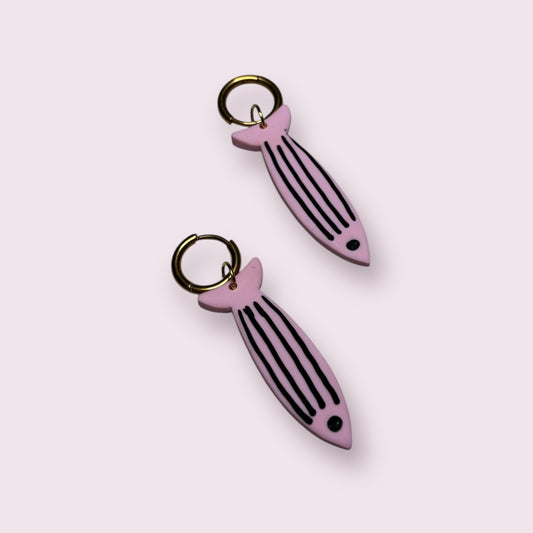 Pendientes con forma de sardina en color rosa pastel con rayas negras, hechos a mano en arcilla polimérica por Aroa Dedales. Diseñados con aro dorado, son el complemento perfecto para looks veraniegos con estilo marinero. Joyas artesanales originales, ligeras y divertidas, ideales para regalar o lucir en vacaciones. Hecho en España con acabado único y creativo para amantes del diseño costero.