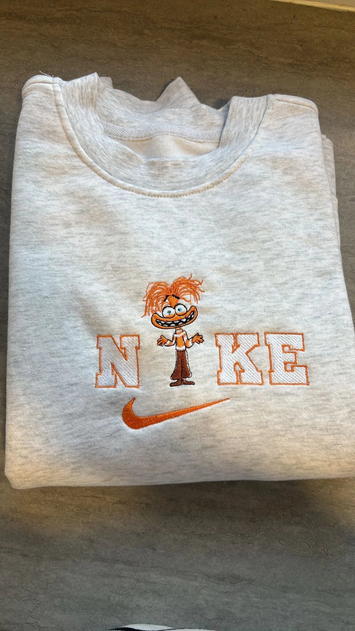 Sudadera viral con bordado del personaje Ansiedad de Inside Out 2 (Del Revés 2). Diseño sobre tela gris con detalles en naranja y el personaje con sus maletas característicos. Sudadera personalizada de Ansiedad, el personaje más popular de la nueva película de Disney Pixar. Ideal para estar a la moda con un look comfy y divertido. Alta calidad en el detalle del bordado.