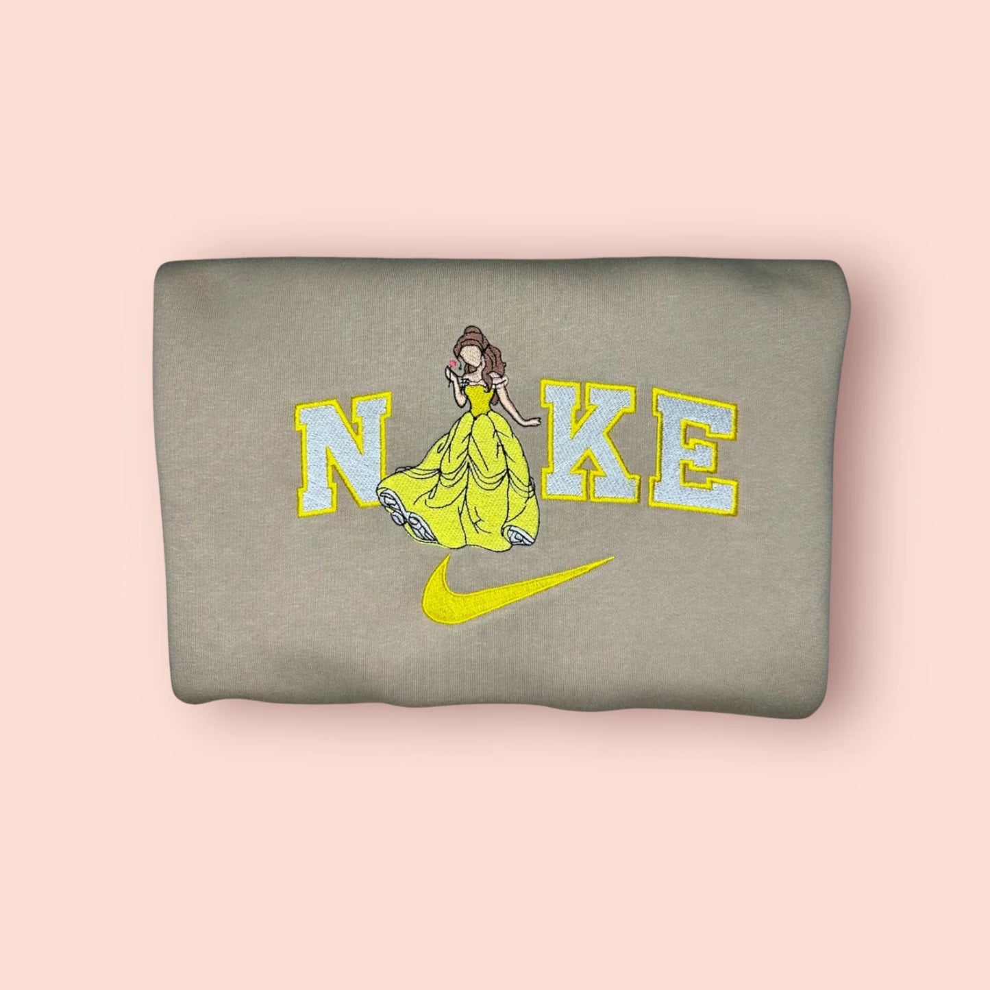 Sudadera de color beige arena con un elegante bordado de la Princesa Bella de "La Bella y la Bestia". El diseño captura el icónico momento del baile con su voluminoso vestido amarillo y la rosa encantada en la mano, integrados en letras estilo universitario en tonos azules y amarillos. Prenda personalizada de alta calidad, perfecta para fans de las Princesas Disney y para crear outfits estilo "Disneybound". Suave, cálida y con detalles mágicos.