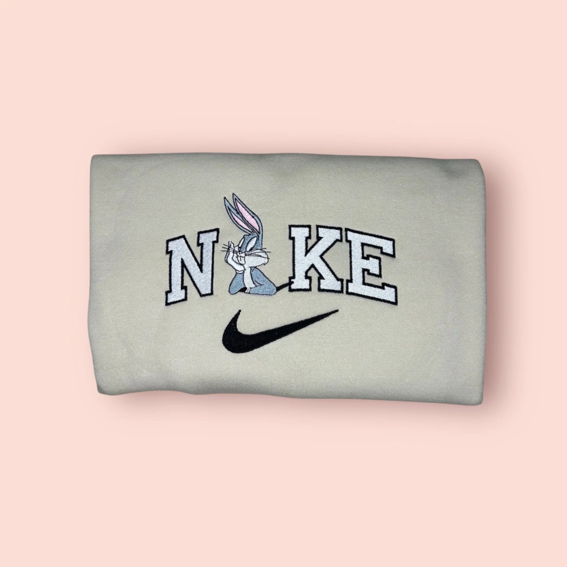 Sudadera de color beige o hueso con un bordado premium de Bugs Bunny. El diseño captura al conejo más famoso en su pose clásica y desenfadada, sobre letras estilo varsity. Prenda de estética retro, ideal para regalar a novios o fans de los dibujos de Warner Bros. El 'Player 1' perfecto para combinar con la sudadera de Lola Bunny y preguntar juntos: "¿Qué hay de nuevo, viejo?".