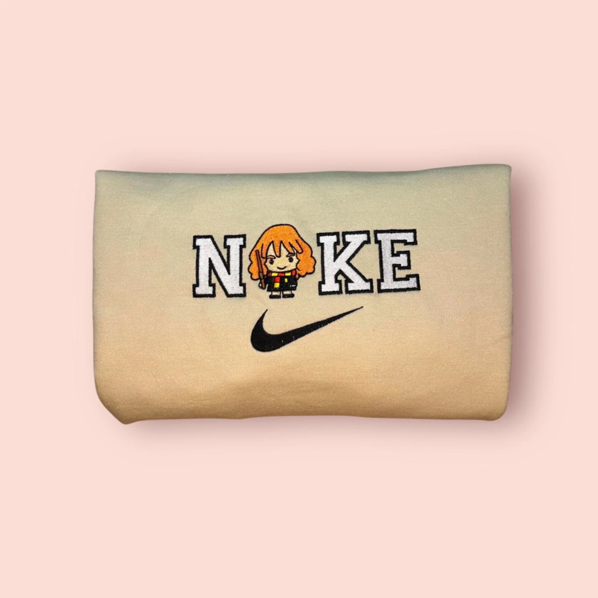 Sudadera de color beige arena con un adorable bordado estilo "chibi" de Hermione Granger. El diseño muestra a la bruja más brillante de su edad con el uniforme de Hogwarts, su varita y la bufanda de Gryffindor, integrada en letras estilo universitario. Ropa personalizada de Harry Potter, ideal para fans que buscan un estilo mágico y cómodo. El regalo perfecto para esa amiga que siempre tiene la solución a todo.