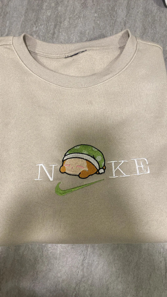 Sudadera color beige arena con un tierno bordado de Waddle Dee durmiendo. Este adorable personaje del universo Kirby lleva su gorrito verde a juego. Una prenda exclusiva para fans de Nintendo que buscan algo diferente al clásico Kirby rosa. Ideal para comprar en pack junto a la sudadera de Kirby y hacer un "matching outfit" de sueño y relax.