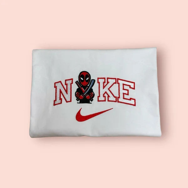 Sudadera blanca de estilo urbano con un bordado exclusivo de Deadpool (Wade Wilson) de Marvel. El diseño muestra al "Mercenario Bocazas" en versión chibi cruzando sus katanas, integrado en letras rojas estilo universitario deportivo. Sudadera personalizada de alta calidad, perfecta para fans de los cómics y superhéroes. El regalo friki ideal, cómodo y con mucho estilo para llevar al cine o usar a diario.
