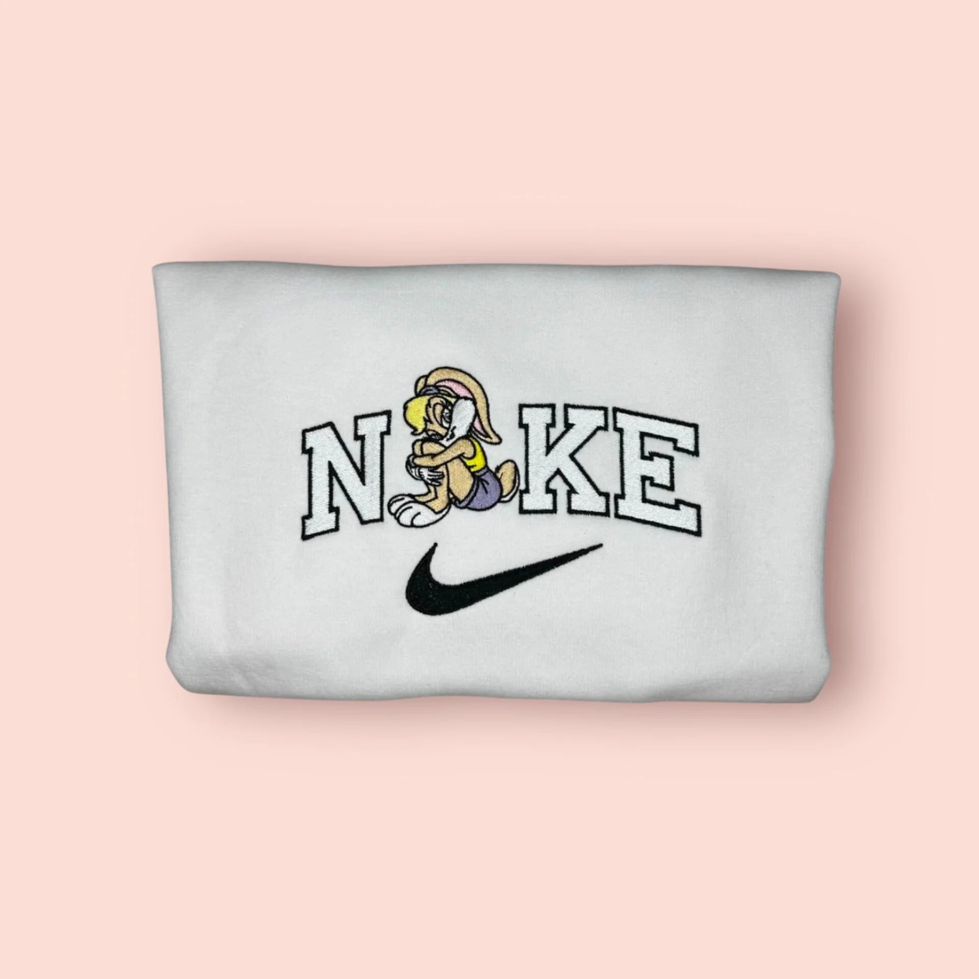 Sudadera blanca de algodón con un bordado exclusivo de Lola Bunny. El diseño muestra al personaje de Looney Tunes en una pose coqueta, integrado en letras estilo universitario. Ropa personalizada inspirada en la película Space Jam y la estética de los 90. La prenda perfecta para chicas con carácter que saben que no son una "muñeca". Cómprala junto a la de Bugs Bunny y formad el mejor equipo del Tune Squad.