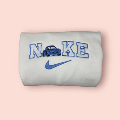 Sudadera blanca de alta calidad con un elegante bordado de Sally Carrera de la película Cars. El diseño presenta al Porsche azul integrado en letras estilo universitario con hilos a juego. Prenda de moda personalizada, perfecta para fans de Disney y Pixar. Ideal para regalar o para combinar con la sudadera de Rayo McQueen y crear el conjunto de pareja definitivo.