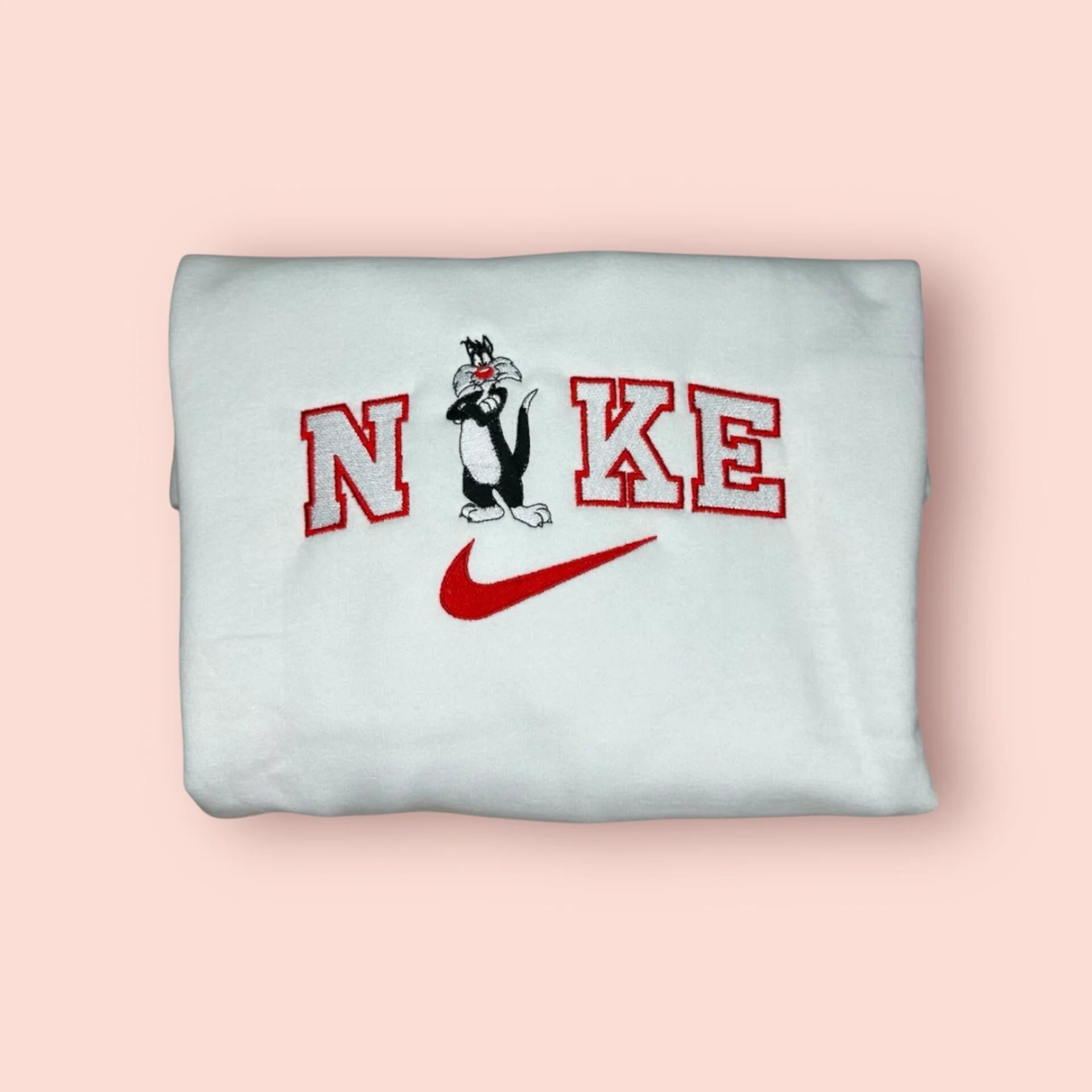 Sudadera blanca de estilo varsity con un bordado detallado del Gato Silvestre de los Looney Tunes. El diseño presenta al personaje con su clásica expresión de "haber visto un lindo gatito", integrado en letras rojas estilo universitario. Ropa personalizada de estética vintage y noventera (90s aesthetic). El regalo perfecto para nostálgicos de los dibujos animados clásicos o para combinar en pareja con la sudadera de Piolín. Tejido de algodón de alta calidad y bordado duradero.