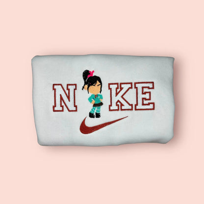 Sudadera blanca de estilo deportivo con un bordado exclusivo de Vanellope von Schweetz de la película ¡Rompe Ralph! (Wreck-It Ralph). El diseño muestra a la princesa de Sugar Rush con su característica sudadera verde azulado y falda de "papelito", integrada en el logo con actitud desafiante. Ropa personalizada "Glitch" ideal para chicas gamers y fans de Disney. El regalo perfecto para combinar con la sudadera de Ralph.