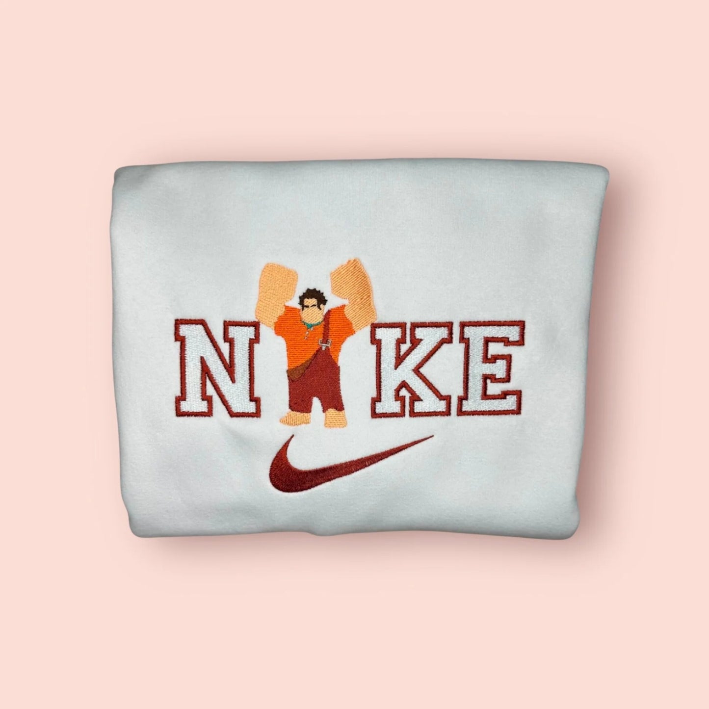 Sudadera blanca con un imponente bordado de Ralph el Demoledor (Rompe Ralph). El diseño captura al personaje con sus puños gigantes y peto naranja, listo para "romperlo todo", sobre letras estilo varsity. Prenda de algodón cómoda y resistente, inspirada en los videojuegos arcade retro. Compra obligada para el "Player 1" de tu vida y crea el conjunto a juego con Vanellope.