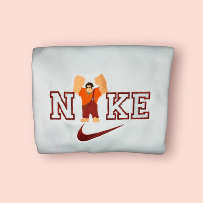 Sudadera blanca con un imponente bordado de Ralph el Demoledor (Rompe Ralph). El diseño captura al personaje con sus puños gigantes y peto naranja, listo para "romperlo todo", sobre letras estilo varsity. Prenda de algodón cómoda y resistente, inspirada en los videojuegos arcade retro. Compra obligada para el "Player 1" de tu vida y crea el conjunto a juego con Vanellope.