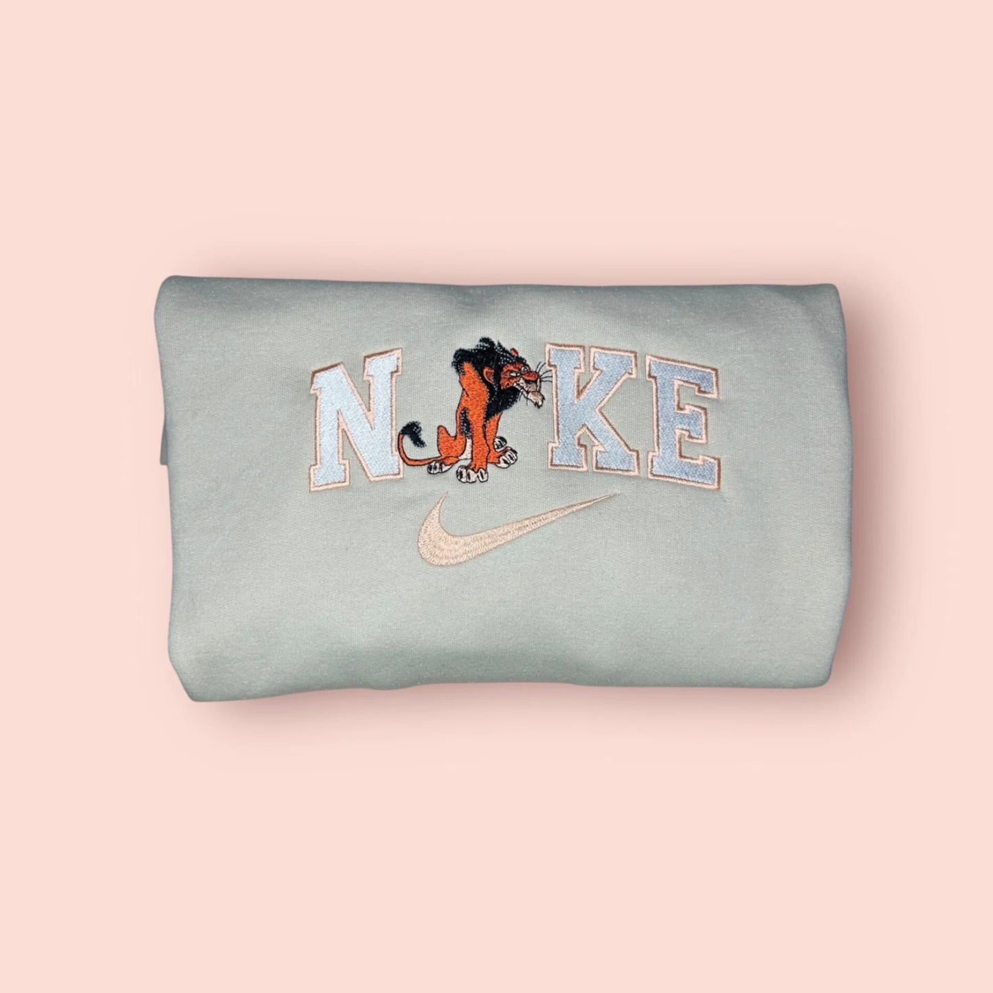 Sudadera de color gris azulado pálido (tono menta suave) con un bordado premium de Scar, el icónico villano de El Rey León. El diseño muestra a Scar con su melena negra y expresión astuta y desafiante, integrado en letras estilo varsity. Ropa personalizada ideal para fans de los Villanos Disney que buscan un estilo con carácter y un toque de rebeldía. Calidad superior, perfecta para un outfit urbano y diferente.
