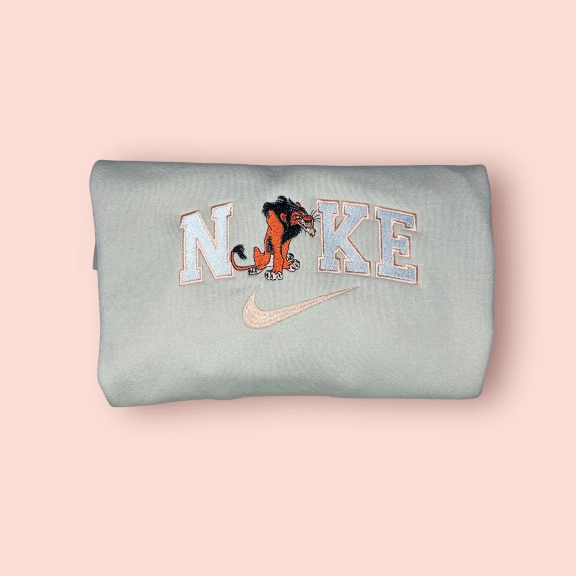 Sudadera de color gris azulado pálido (tono menta suave) con un bordado premium de Scar, el icónico villano de El Rey León. El diseño muestra a Scar con su melena negra y expresión astuta y desafiante, integrado en letras estilo varsity. Ropa personalizada ideal para fans de los Villanos Disney que buscan un estilo con carácter y un toque de rebeldía. Calidad superior, perfecta para un outfit urbano y diferente.
