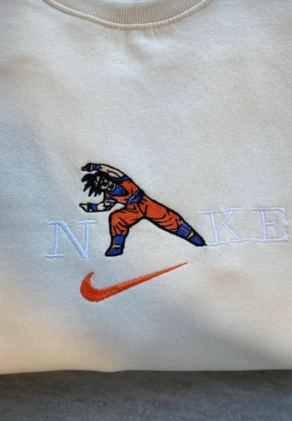 Sudadera de color crema o hueso con un bordado dinámico de Son Goku de Dragon Ball Z. El diseño muestra al legendario Saiyan en su pose de combate, integrado sobre letras estilo universitario. Ropa anime de alta calidad (Anime Streetwear), ideal para fans de la saga de Akira Toriyama. El regalo perfecto para el "Kakarot" de tu vida, y la pieza clave para combinar con la sudadera de Vegeta.