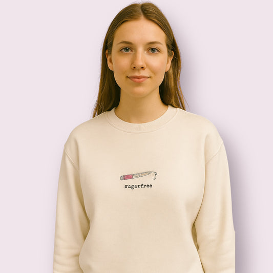 Mujer joven con sudadera beige con diseño bordado de una pluma de insulina y la frase "sugarfree", ideal para personas con diabetes tipo 1 que buscan ropa con mensajes positivos. Moda inclusiva y conciencia diabética en ropa cómoda y original
