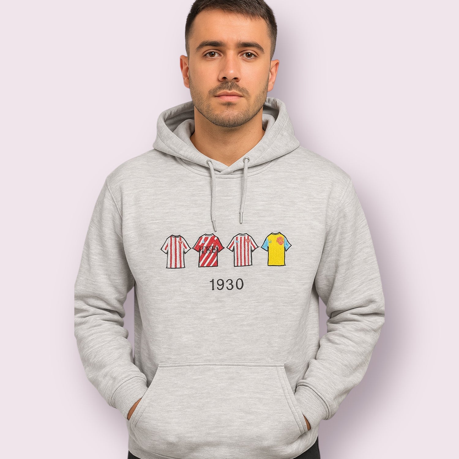 Sudadera gris con capucha de diseño exclusivo para aficionados del Girona FC, con bordado de camisetas históricas del club en distintas versiones a rayas rojas y blancas, junto con la camiseta amarilla suplente y el número 1930 como referencia a la fundación del equipo. Ideal para mostrar orgullo gironí con estilo moderno y cómodo, perfecta para fans del fútbol español.