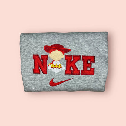 Sudadera gris jaspeado con un vibrante bordado rojo de Jessie, la vaquera de Toy Story. El diseño presenta la silueta del personaje con su icónico sombrero y trenzas sobre letras estilo universitario. Ropa personalizada ideal para chicas fans de Disney Pixar. Compra esta sudadera para combinar con el modelo de Woody y crear el outfit de pareja perfecto. Tejido suave y resistente.