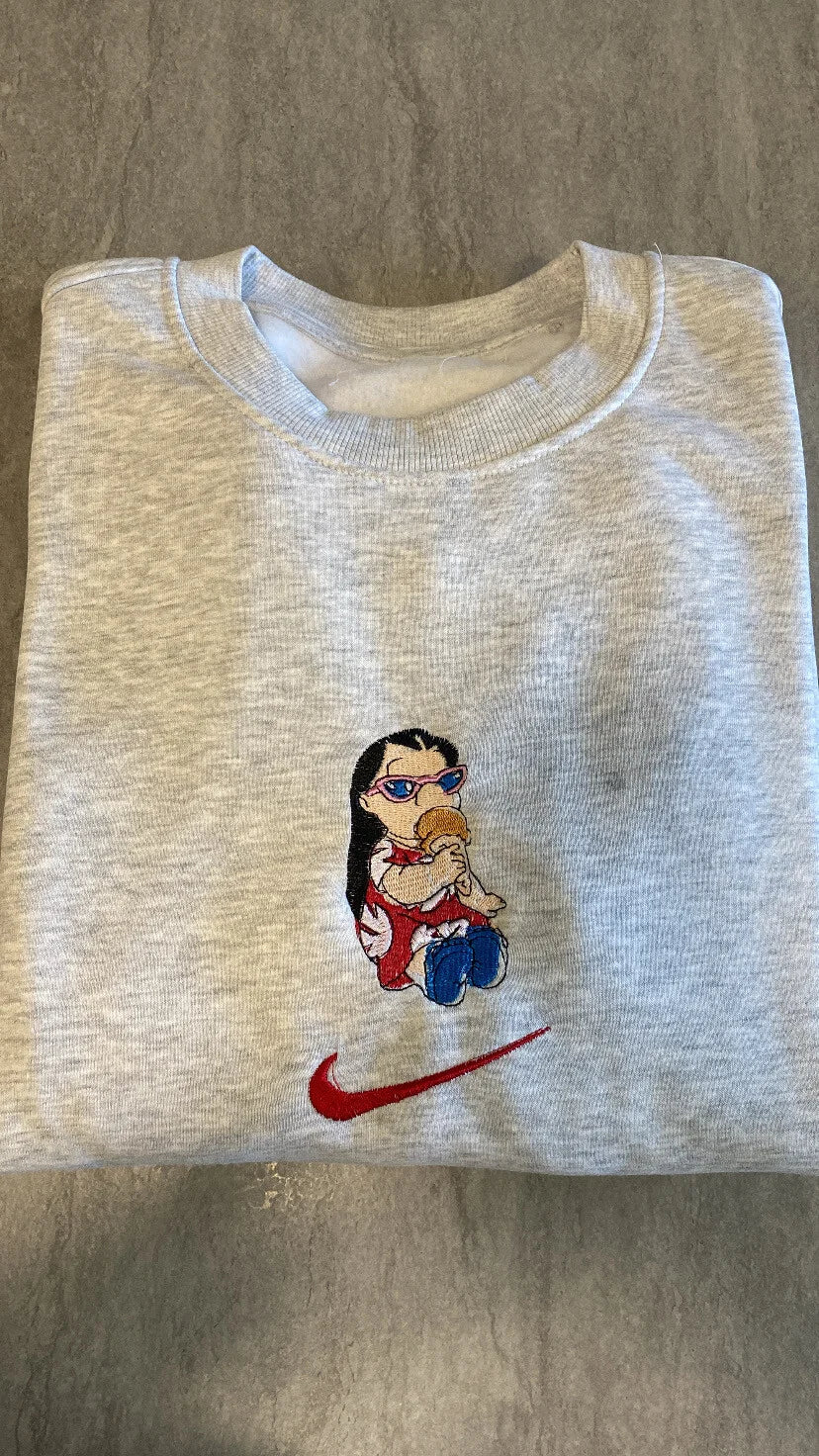 Sudadera de color gris jaspeado con un bordado exclusivo de Lilo Pelekai. El diseño muestra a la icónica niña hawaiana con sus gafas de sol comiéndose un bocadillo de mermelada, justo encima del logo. Ropa personalizada de Lilo & Stitch, perfecta para regalar a tu mejor amiga o hermana. Combínala con la sudadera de Stitch para crear el "matching outfit" de "Ohana" definitivo.