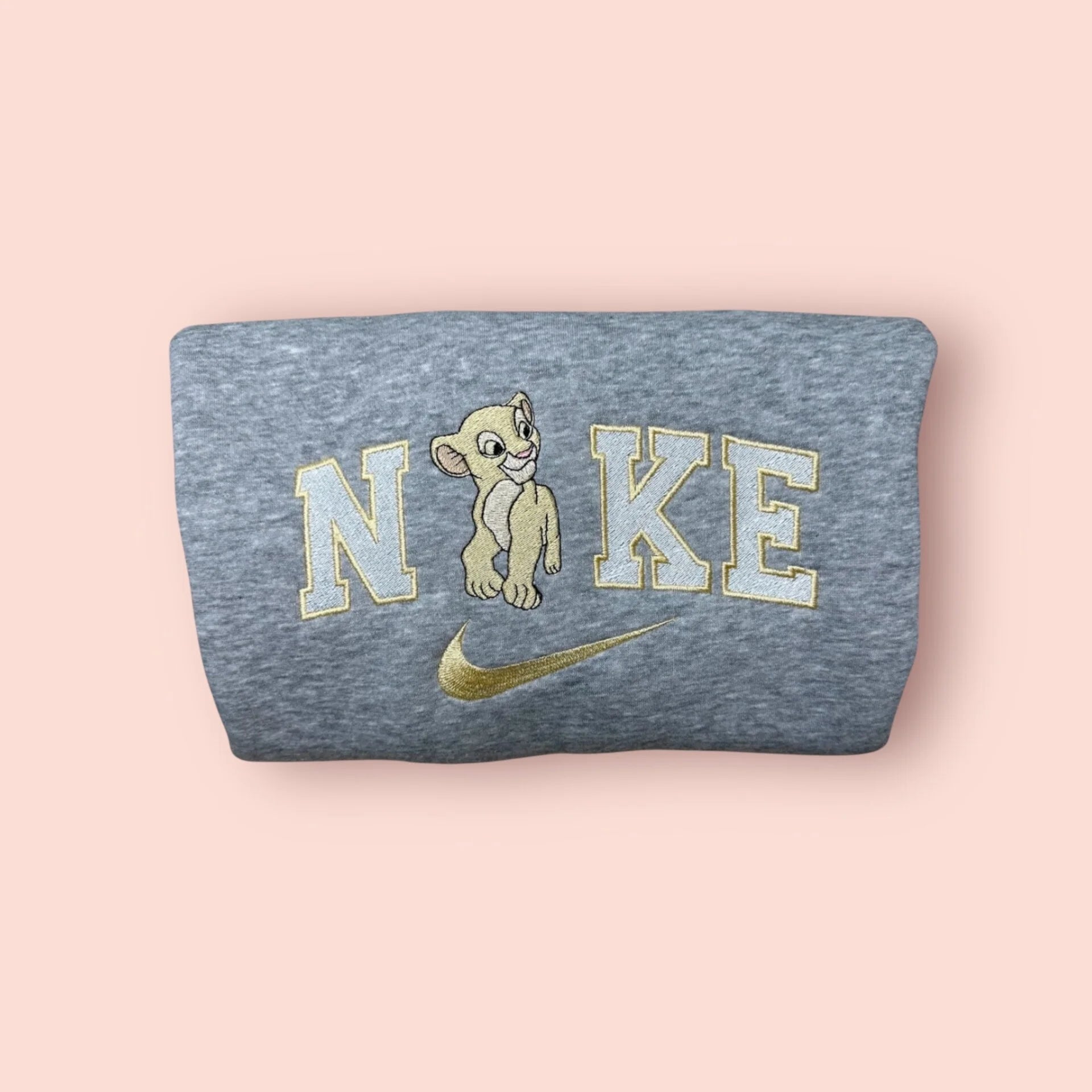 Sudadera de color gris jaspeado con un bordado dulce y detallado de Nala (cachorra) de El Rey León. Diseño con hilos en tonos crema y dorados sobre letras estilo universitario. Ropa personalizada de alta calidad, suave y cálida. El regalo perfecto para ella, ideal para crear un conjunto a juego con la sudadera de Simba. Moda Disney discreta y elegante.