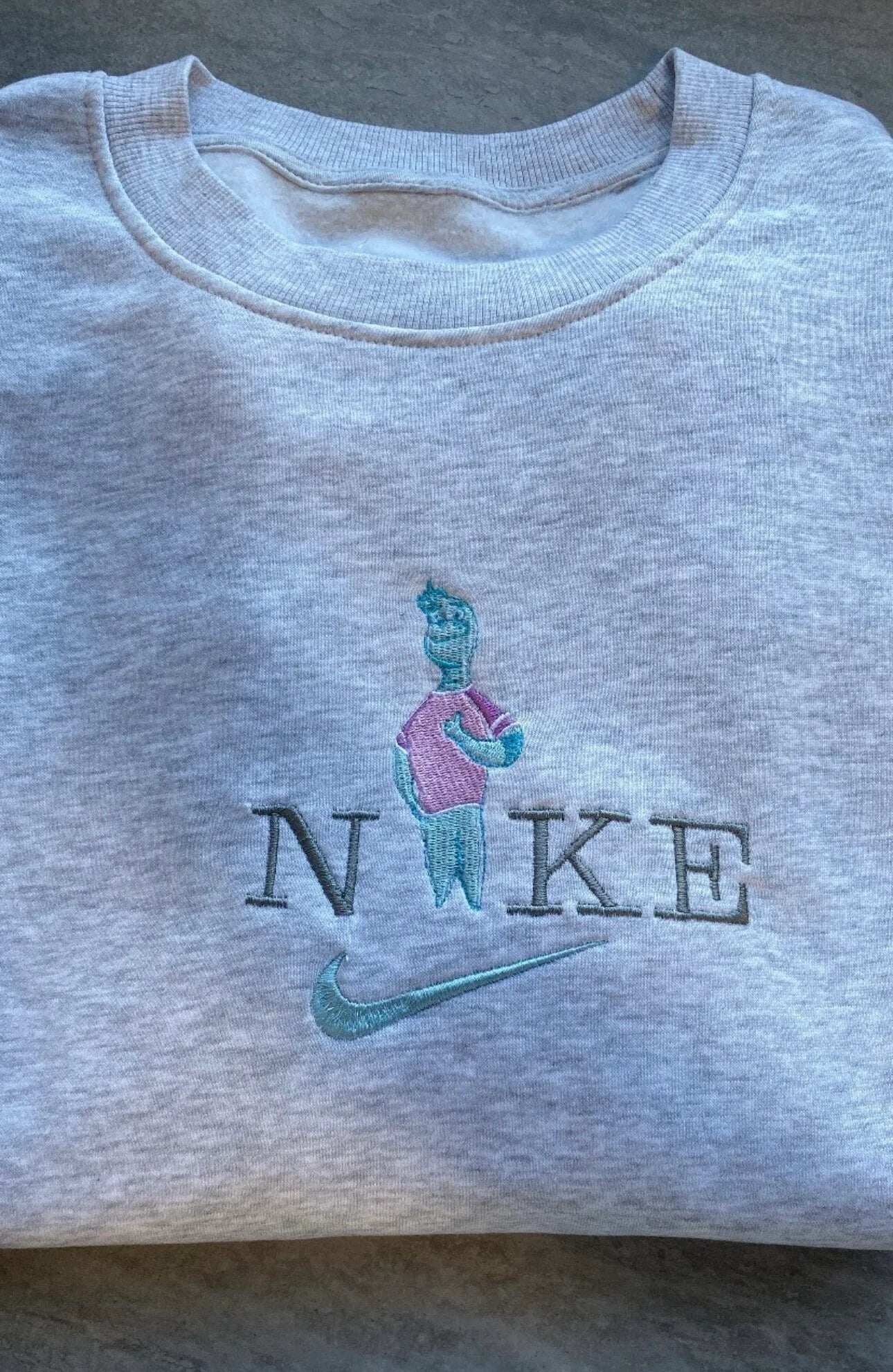 Sudadera gris jaspeado con un bordado detallado de Nilo (Wade Ripple) de la película Elementos. El diseño captura al sensible personaje de agua con sus tonos turquesa y rosa, integrado en el logo. Prenda de Pixar perfecta para regalar a novios o para crear el conjunto de pareja más original. La pieza que completa el dúo "Fuego y Agua" con la sudadera de Candela.