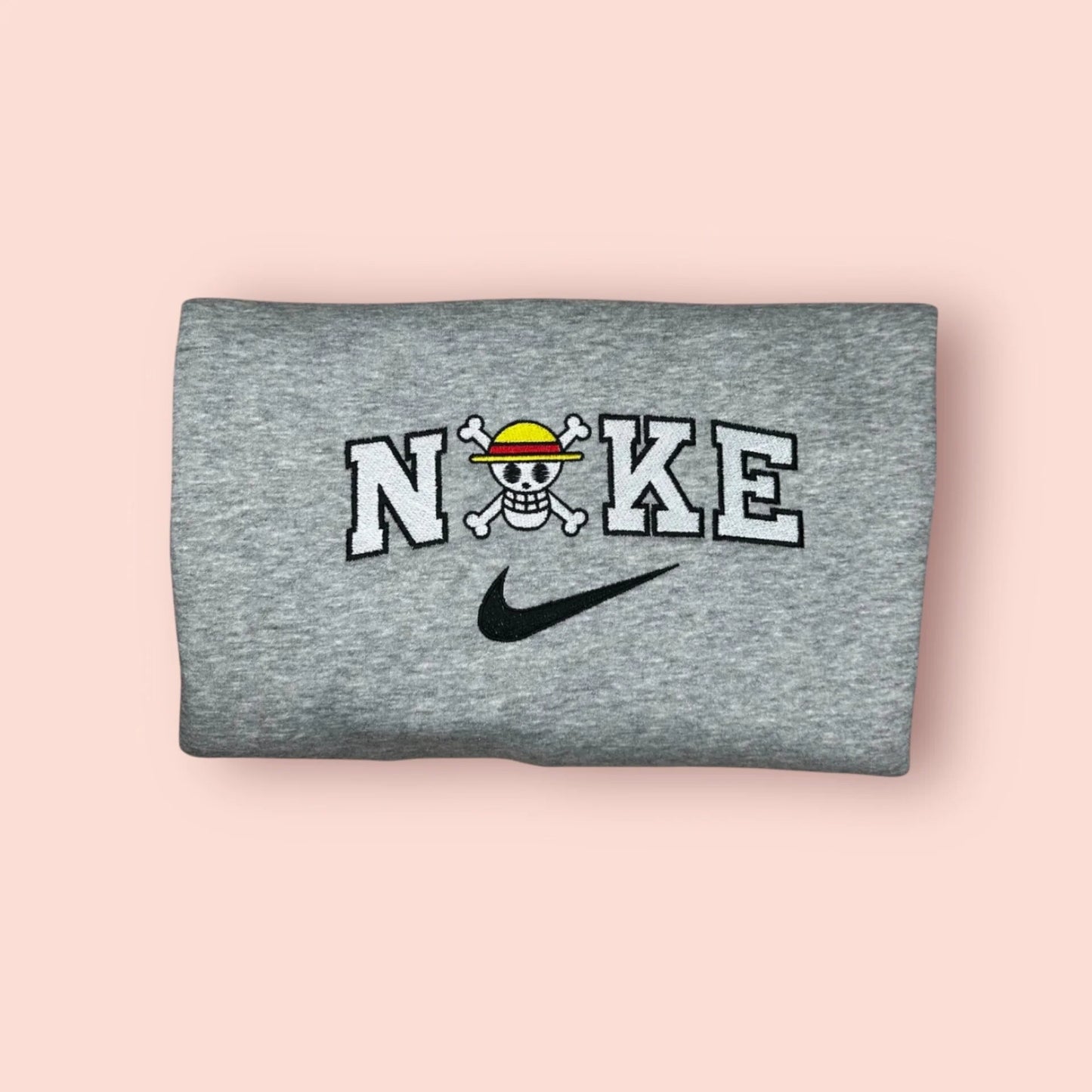 Sudadera de color gris jaspeado con un bordado minimalista y limpio de la Jolly Roger de los Sombrero de Paja (Mugiwara). El diseño integra la icónica calavera de Luffy con su sombrero de paja dentro de un logo estilo deportivo (letras blancas y negras). Ropa anime "streetwear" de alta calidad, ideal para fans de One Piece que buscan merchandising discreto y elegante. El regalo perfecto para cualquier Nakama que aspira a ser el Rey de los Piratas.