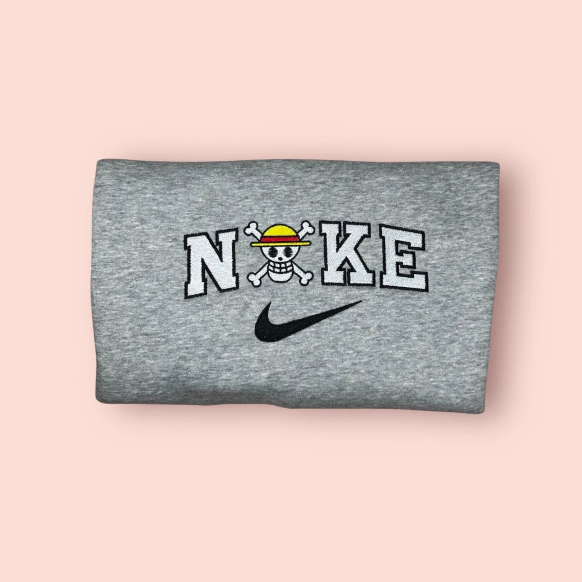 Sudadera de color gris jaspeado con un bordado minimalista y limpio de la Jolly Roger de los Sombrero de Paja (Mugiwara). El diseño integra la icónica calavera de Luffy con su sombrero de paja dentro de un logo estilo deportivo (letras blancas y negras). Ropa anime "streetwear" de alta calidad, ideal para fans de One Piece que buscan merchandising discreto y elegante. El regalo perfecto para cualquier Nakama que aspira a ser el Rey de los Piratas.