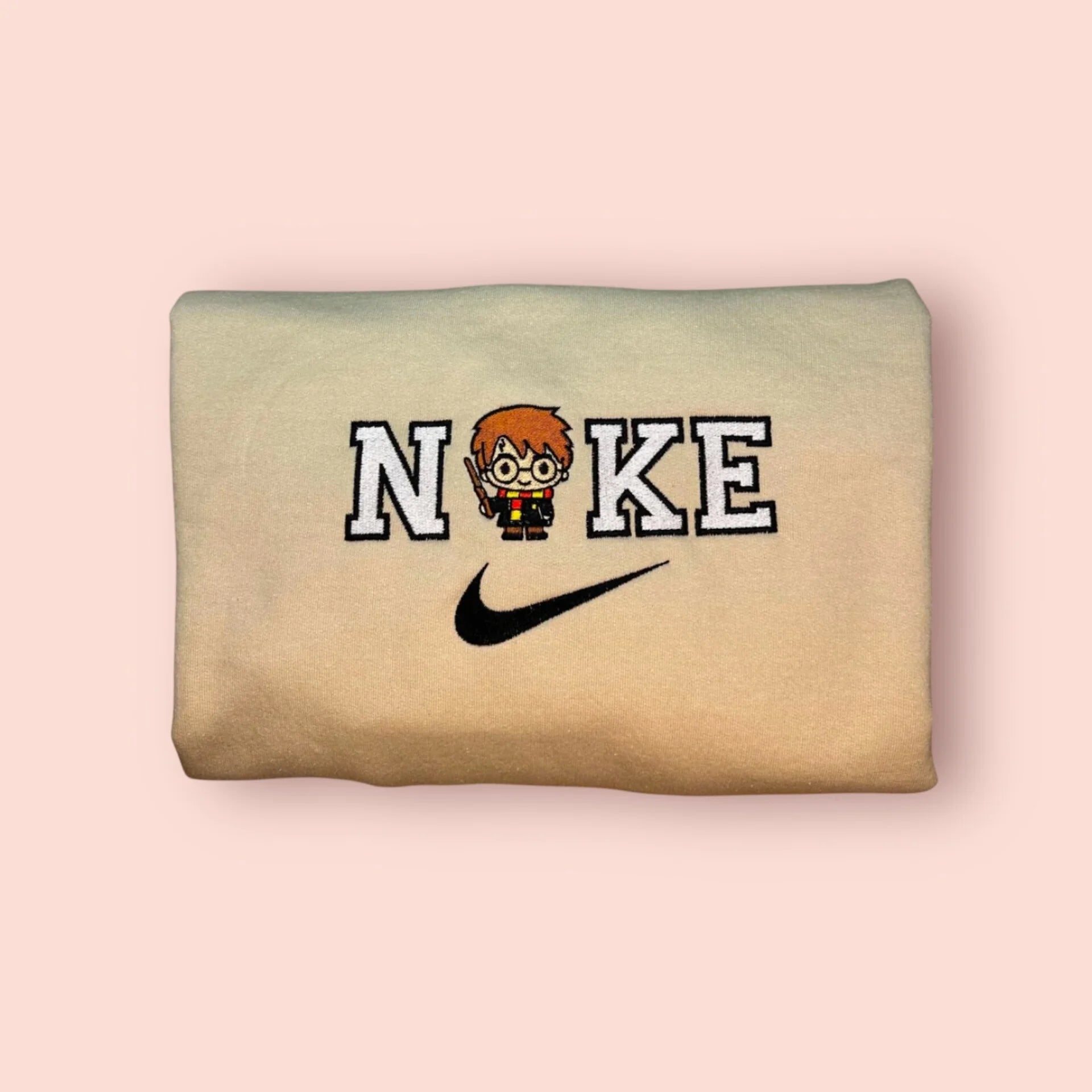 Sudadera beige de alta calidad con bordado detallado de Harry Potter. El diseño destaca las icónicas gafas redondas, la cicatriz de rayo y la bufanda granate y dorada de Gryffindor. Prenda de estilo deportivo (varsity) para hombres o unisex. Compra este básico del Mundo Mágico para combinar con la sudadera de Hermione y crear el look de "Hogwarts Alumni" definitivo.