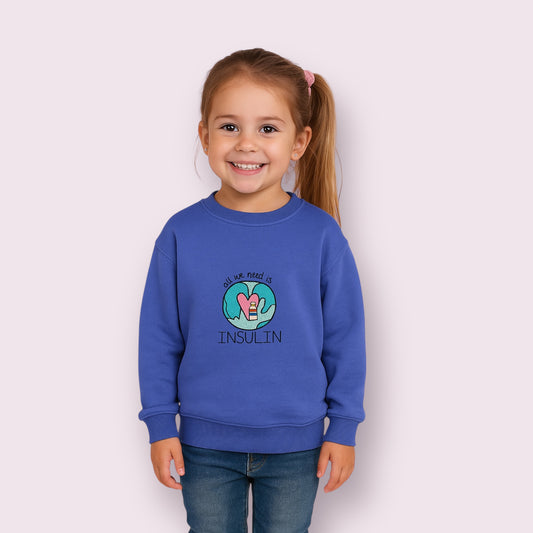 Niña sonriente vestida con sudadera azul de algodón con bordado "All we need is insulin", diseñada para niños y niñas con diabetes tipo 1. Moda infantil inclusiva y con conciencia, perfecta para el día a día