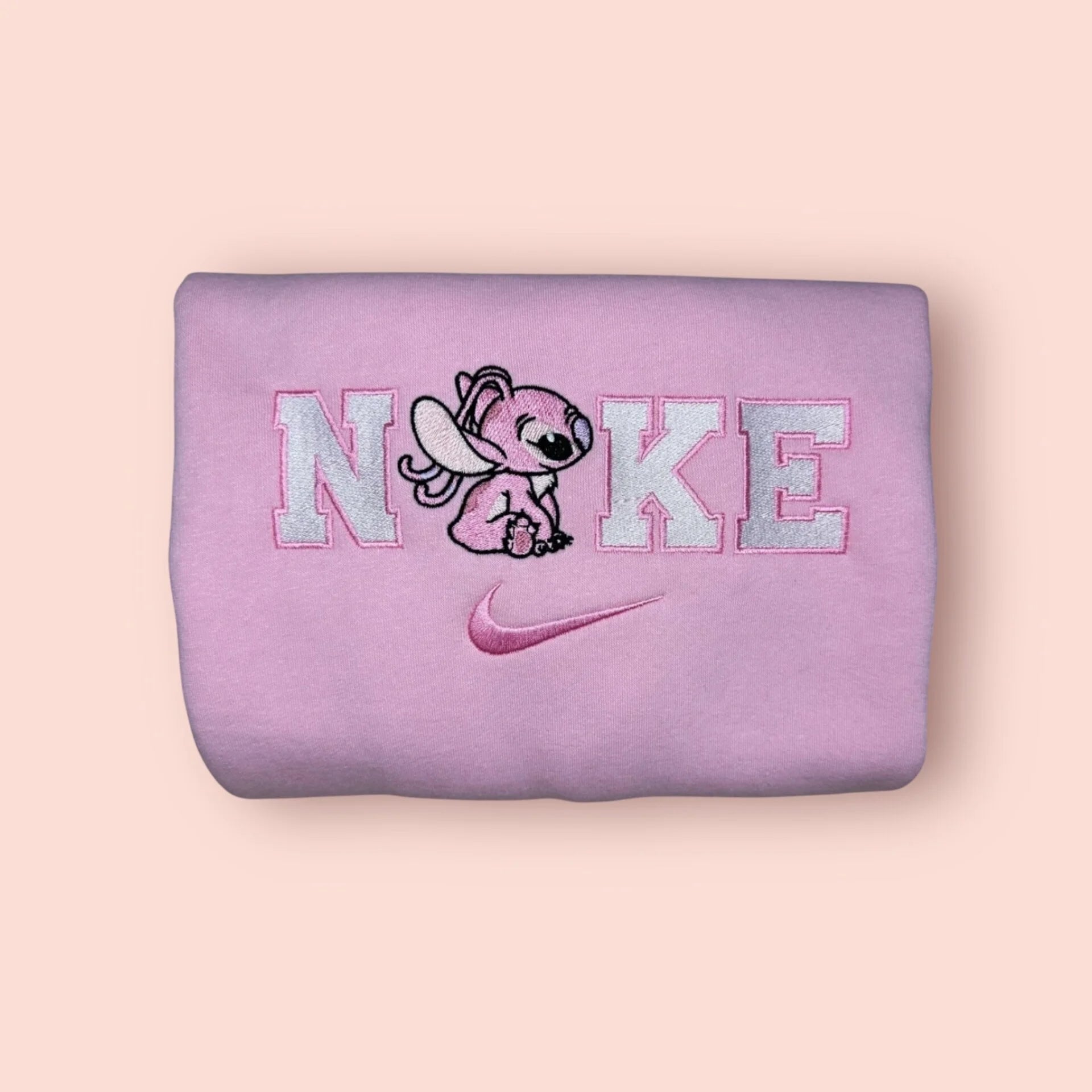 Sudadera de color rosa pastel con un bordado adorable de Ángela (Angel/Experimento 624), la novia de Stitch. El diseño muestra al personaje en una pose tierna integrado en letras estilo universitario con hilos blancos y rosas. Ropa personalizada "kawaii" de Disney, perfecta para chicas. El regalo de San Valentín ideal para combinar con la sudadera azul de Stitch.