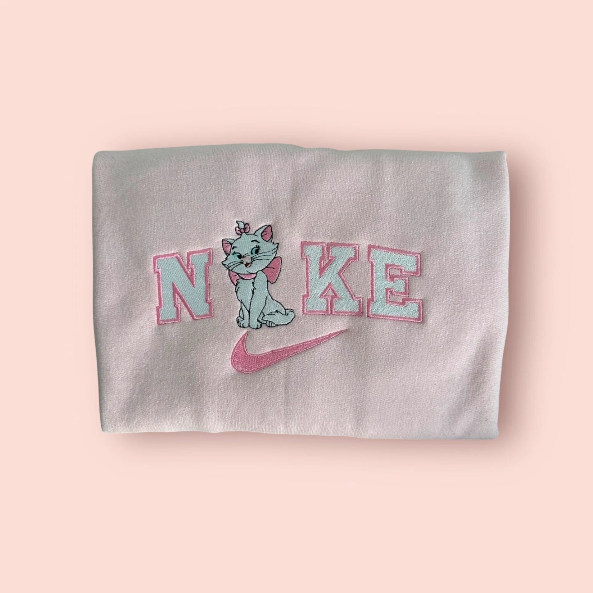 Sudadera de color rosa pastel (baby pink) con un adorable bordado de la gatita Marie de la película Los Aristogatos. El diseño captura la esencia "Coquette" con Marie luciendo su gran lazo rosa y su expresión coqueta y elegante, integrada en letras estilo universitario. Ropa personalizada Disney de alta calidad, suave y femenina. El regalo perfecto para amantes de los gatos y chicas con estilo que saben que "las damas no empiezan las peleas, pero saben terminarlas".