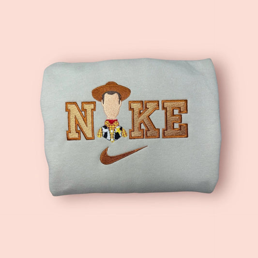 Sudadera color piedra o gris claro con bordado detallado del Sheriff Woody de Toy Story. Diseño exclusivo con tonos tierra y dorados, mostrando la placa de sheriff y el sombrero de vaquero. Sudadera personalizada de "Tu Amigo Fiel", perfecta para regalar a novios o fans de la saga. Combínala con la sudadera de Jessie para un look de "goals" en pareja. Calidad premium en cada puntada.