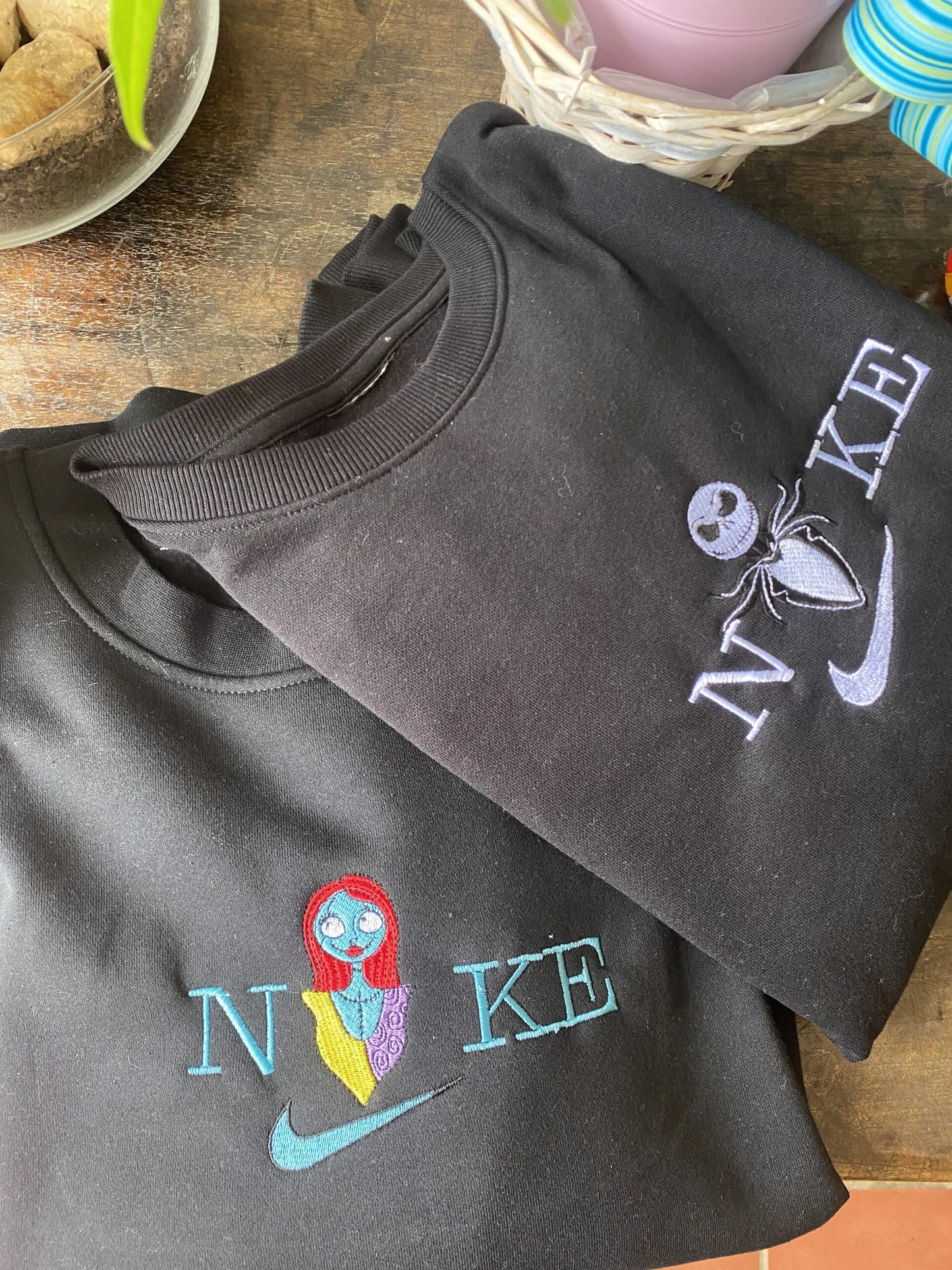 Dos sudaderas negras bordadas de Jack Skellington y Sally, la pareja icónica de "Pesadilla Antes de Navidad" de Tim Burton. El diseño de Jack, el Rey Calabaza, se muestra en blanco y negro, mientras que el de Sally resalta con sus colores de muñeca de trapo. Ropa gótica perfecta para parejas que buscan un "matching outfit" para Halloween o Navidad. El regalo ideal para fans que saben que su amor está "destinado a ser".