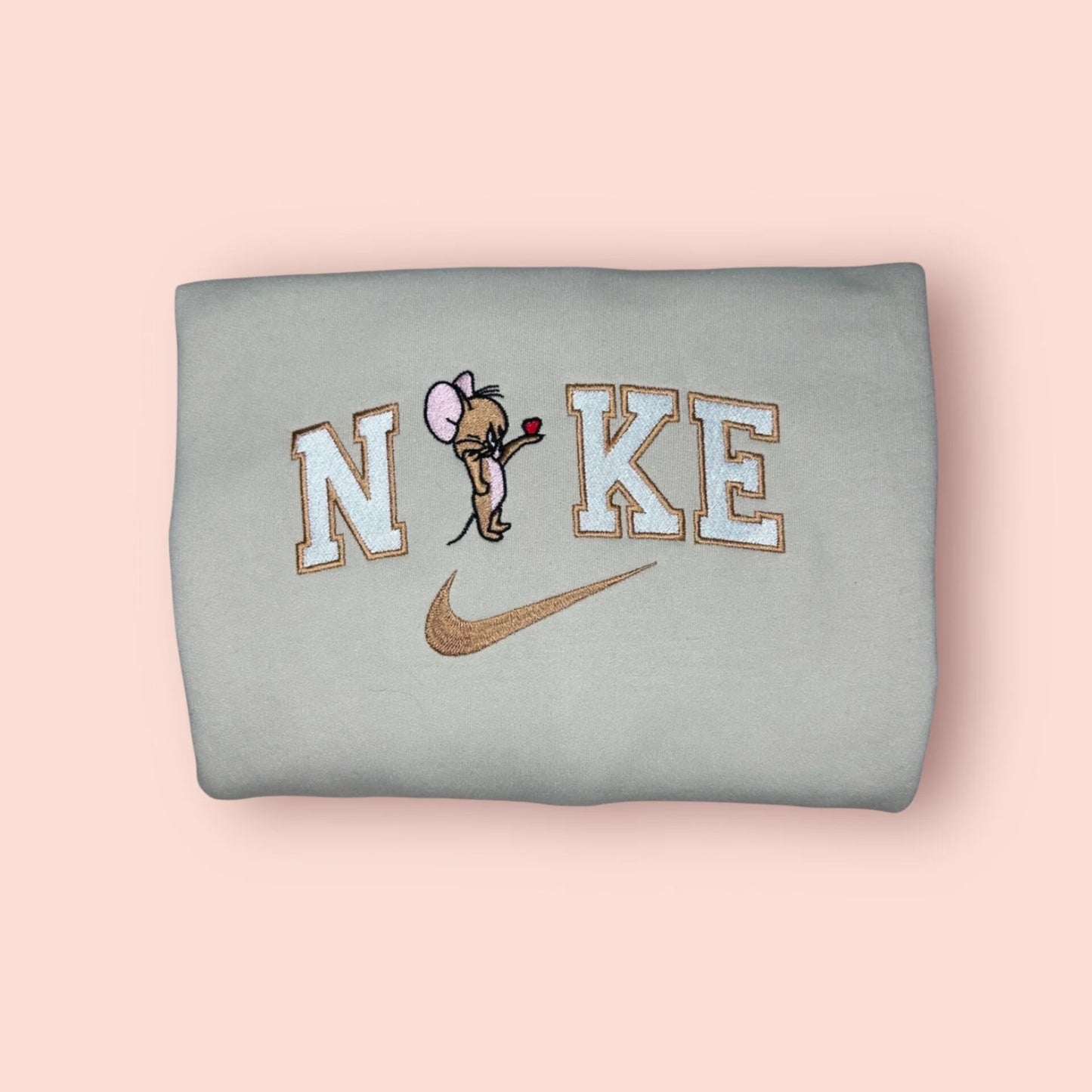 Sudadera de color beige arena con un adorable bordado de Jerry. El famoso ratón de "Tom y Jerry" aparece en una pose dulce ofreciendo un corazón, integrado en letras estilo universitario. Ropa personalizada de estética retro y minimalista. Es el regalo perfecto para la parte tierna y astuta de la relación. Ideal para combinar con la sudadera de Tom y crear el 'matching outfit' definitivo.