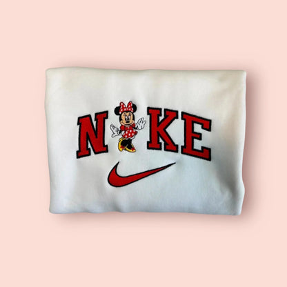 Sudadera blanca impoluta con un bordado vibrante de la clásica Minnie Mouse. El diseño destaca su icónico vestido rojo de lunares y el lazo a juego, integrada con elegancia en letras estilo universitario rojas y negras. Ropa personalizada imprescindible para cualquier viaje a los parques Disney. El regalo perfecto para ella, femenina y atemporal. Combínala con la sudadera de Mickey para el "matching outfit" definitivo.