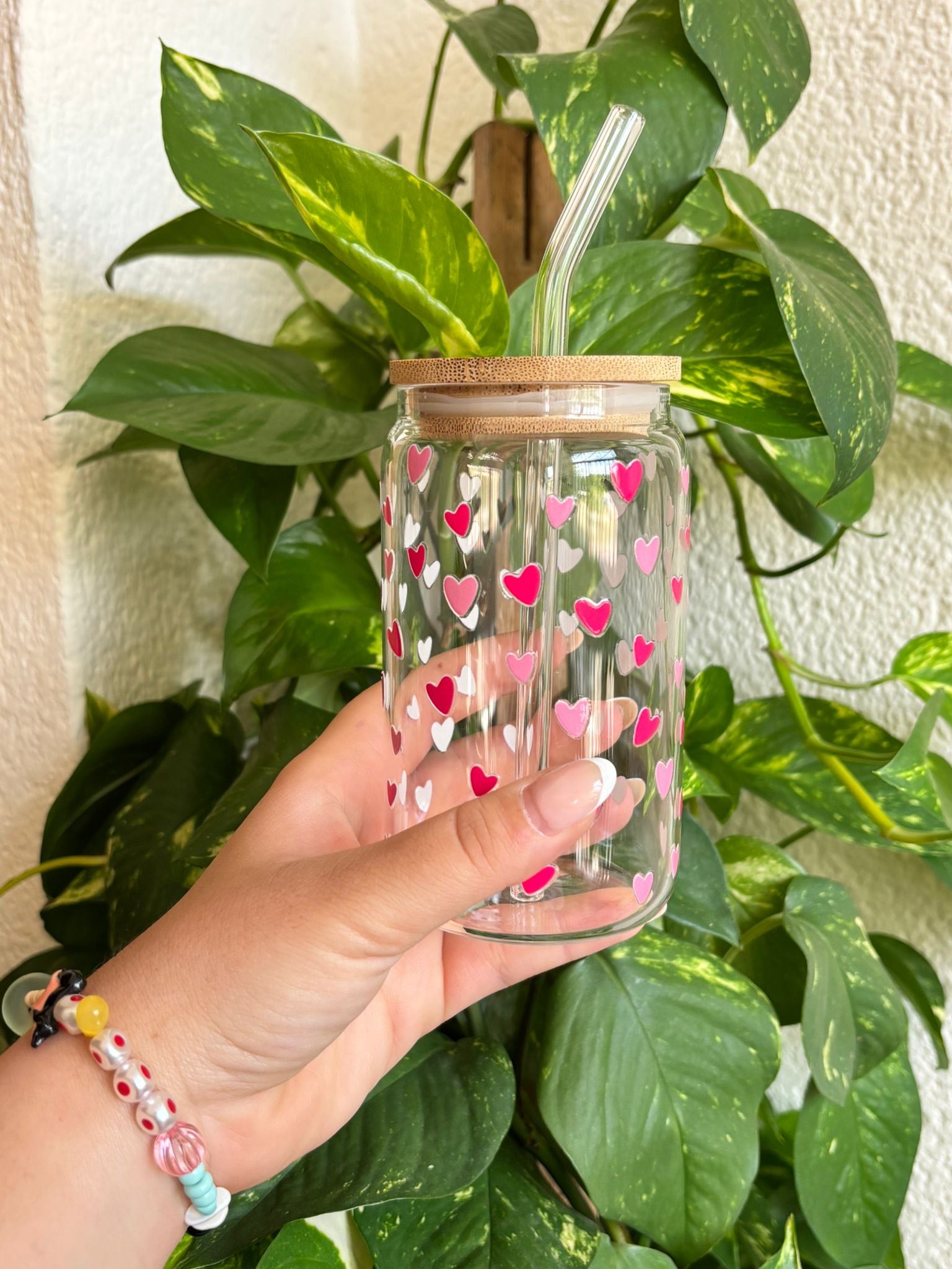Vaso de cristal reutilizable decorado con corazones rosas y blancos, con tapa de bambú ecológica y pajita de cristal curvada. Diseño romántico ideal como regalo original para parejas, amigas o profesoras. Perfecto para bebidas frías como café helado o batidos. Un detalle artesanal y sostenible hecho con mimo, ideal para quienes buscan estilo y funcionalidad en su día a día.
