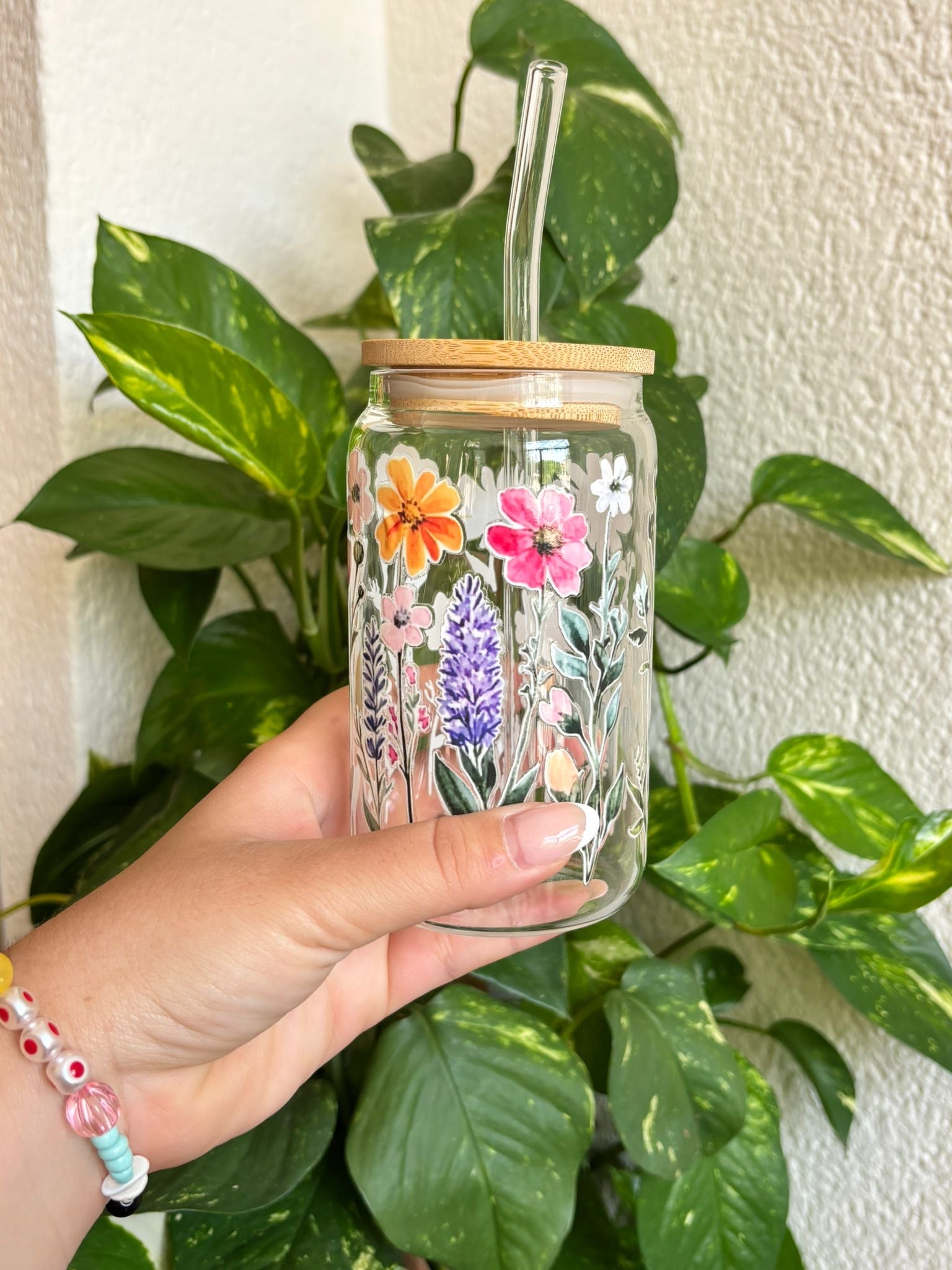 Vaso de cristal decorado con ilustraciones de flores silvestres en colores vivos, con tapa de bambú natural y pajita de cristal reutilizable. Ideal para amantes de la naturaleza y la primavera. Perfecto para smoothies, infusiones frías o cafés con hielo. Un regalo sostenible, bonito y funcional, pensado para profes, amigas o días soleados con estilo floral.