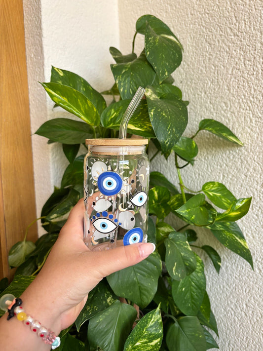 Vaso de cristal con diseño de ojos turcos en tonos azules y blancos, símbolo de protección contra el mal de ojo. Incluye tapa de bambú y pajita de vidrio reutilizable, ideal para bebidas frías como café helado, smoothies, kombucha o agua con limón. Un regalo original y artesanal que combina estilo boho, energía positiva y sostenibilidad.